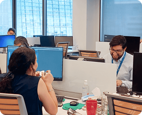 Personas trabajando en una oficina abierta, conversando y usando computadores en un entorno corporativo