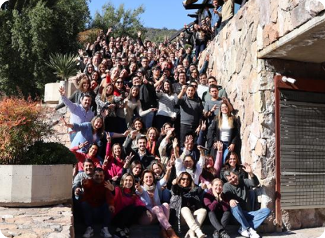 Gran grupo de colaboradores posando y levantando las manos durante una actividad al aire libre