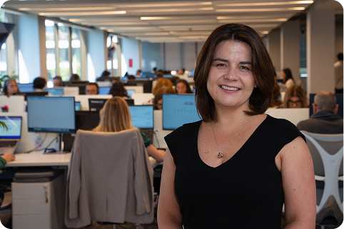 Colaboradora de BICE posando frente a un área operativa de oficina abierta con equipos trabajando