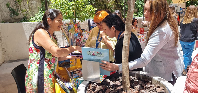 Personas participando en una feria comunitaria, conversando y revisando productos en un stand al aire libre